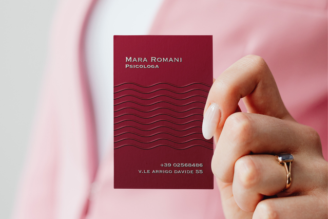 Woman in pink blazer holding wine-red Mara Romani psychologist card with wavy UV relief pattern. Sprint24.